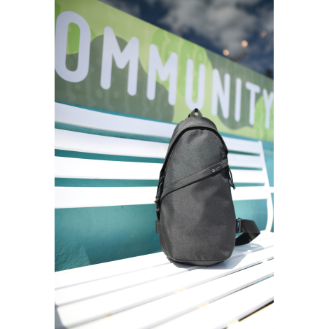 Sac bandoulière recyclé AWARE™ Renew posé en extérieur sur un banc