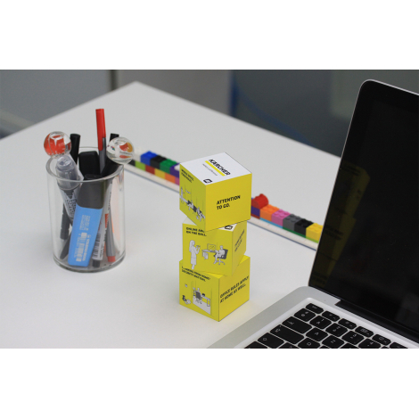 Trois cubes jaunes empilés près d’un pot à stylos, avec visuels sur toutes les faces
