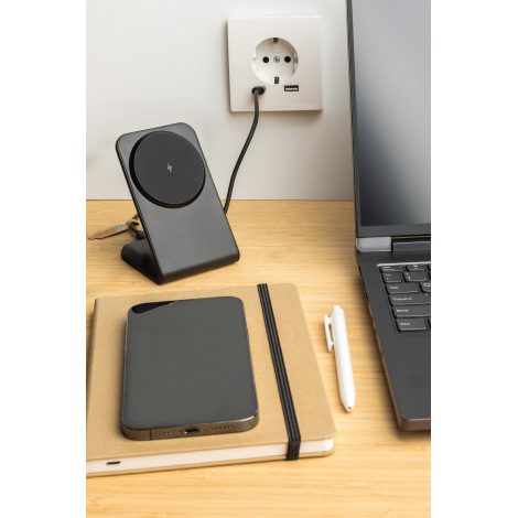 Chargeur magnétique 15W noir recyclé posé sur un bureau branché à une prise murale, smartphone et ordinateur à proximité.