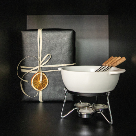 Set à fondue présenté dans un décor festif avec un cadeau emballé en arrière-plan, sans personnalisation.