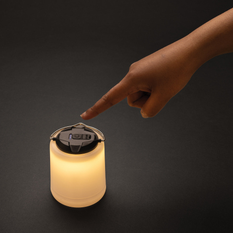 Lampe de table allumée en lumière chaude, posée sur surface sombre avec une main sur le bouton, sans personnalisation.