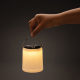 Lampe de table allumée tenue par son anse métallique, sans marquage.