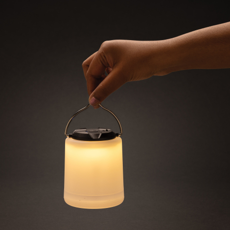 Lampe de table allumée tenue par son anse métallique, sans marquage.