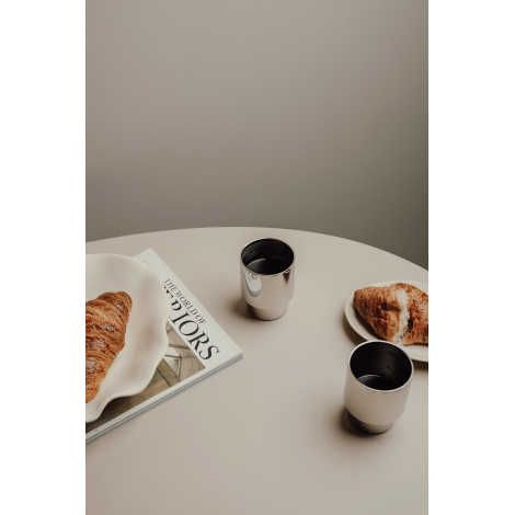 Deux tasses en métal sur une table, l’une remplie de boisson, avec croissant et magazine.