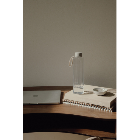 Bouteille translucide sombre sur table en bois près d’un ordinateur et de carnets.