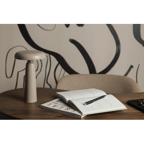 Lampe de table beige posée sur un bureau avec carnet, stylo et magazine, sans marquage visible.