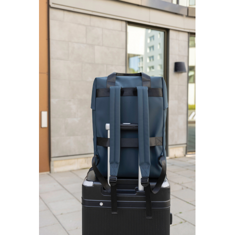 Sac à dos tote bleu fixé sur la poignée d’une valise, vu de dos avec bretelles noires et sangles, sans marquage visible.
