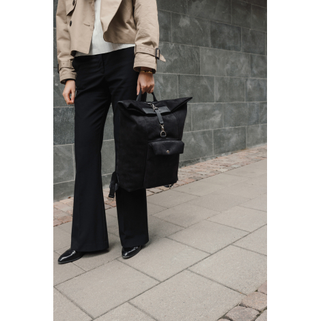 Sac à dos noir porté à la main par une personne en extérieur en tenue urbaine, sans marquage visible.