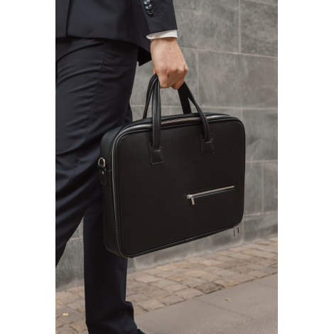 Sacoche noire portée à la main par une personne en tenue de bureau, poche zippée visible, sans marquage visible.
