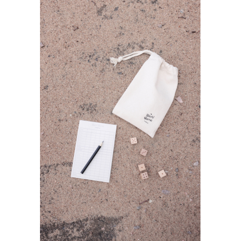 Pochette en coton beige sur sable, avec fiche de score et dés dispersés.
