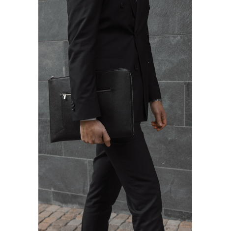 Sacoche ordinateur noire portée à la main par une personne en costume, poche zippée avant visible, sans marquage visible.