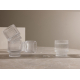Quatre verres rainurés sur une table, deux debout, un incliné et un rempli d’eau.