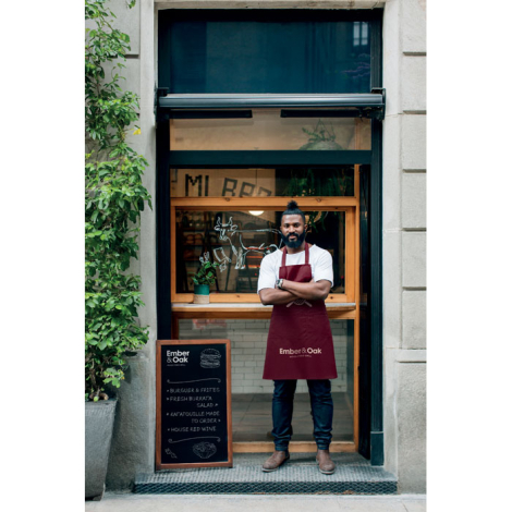 Tablier bordeaux porté devant un restaurant, ajusté à la taille, marquage visible en bas.