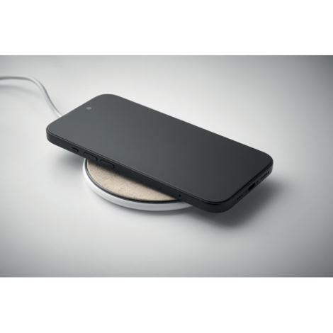Chargeur sans fil rond en liège et textile beige avec smartphone noir posé dessus, sans marquage.