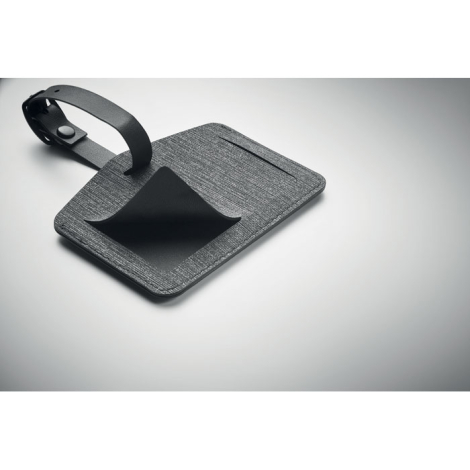 Étiquette de bagage en tissu gris chiné posée à plat avec rabat noir ouvert laissant voir l’emplacement carte, sans marquage.