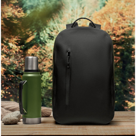 Sac à dos noir en textile posé sur une table extérieure à côté d’une bouteille isotherme verte, sans marquage.