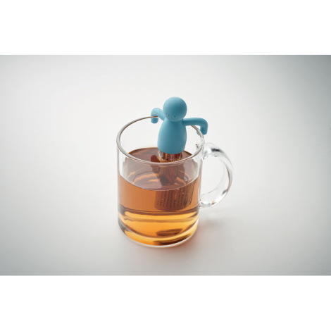 Infuseur à thé bleu posé sur le rebord d’une tasse en verre remplie de thé, sans marquage.