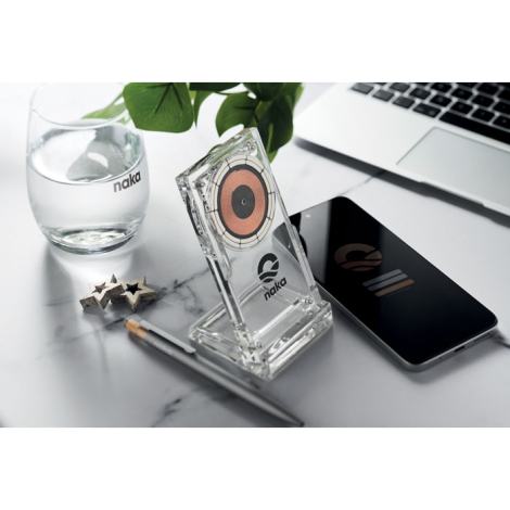 Chargeur sans fil transparent sur un bureau avec smartphone, marquage visible sur le socle avant.