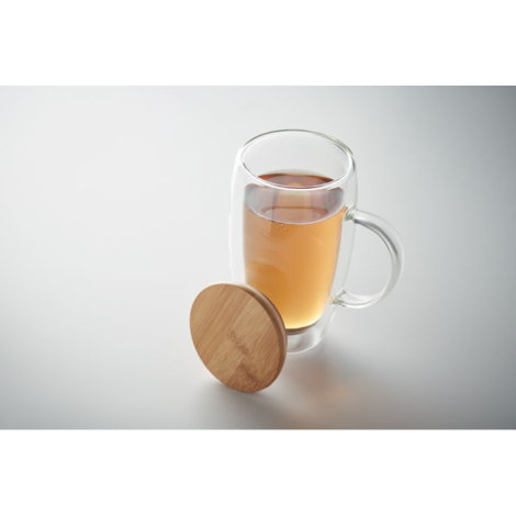Mug en verre double paroi rempli de thé avec couvercle en bambou posé à côté, marquage visible sur le couvercle.