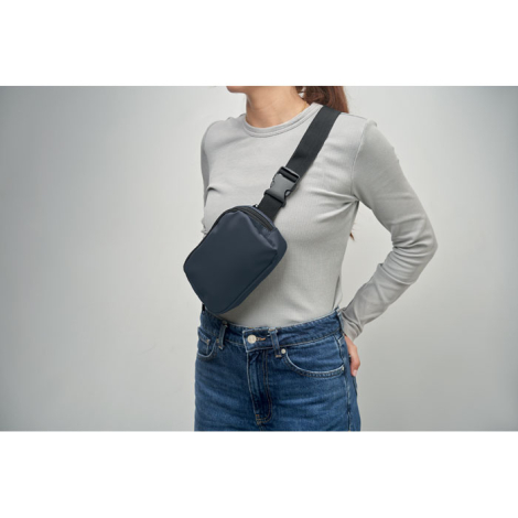 Sac banane bleu foncé porté en bandoulière par une personne en haut gris et jean, sans personnalisation visible.