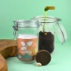 Kit avec deux bocaux en verre, l’un contenant terre et pousse verte, l’autre avec étiquette illustrée et matériel de plantation,