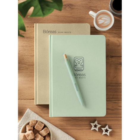 Deux carnets beige et vert posés sur une table avec stylo assorti et tasse de café, marquage visible sur le carnet vert et le st Deux carnets beige et vert posés sur une table avec stylo assorti et tasse de café, marquage visible sur le carnet vert et le st