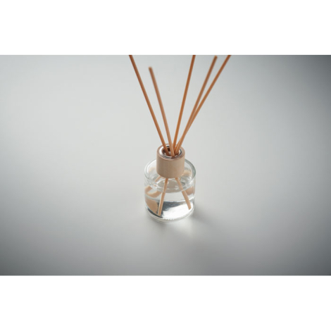 Diffuseur en verre transparent avec bouchon bois clair et tiges de diffusion, photographié en plongée sur fond uni gris.