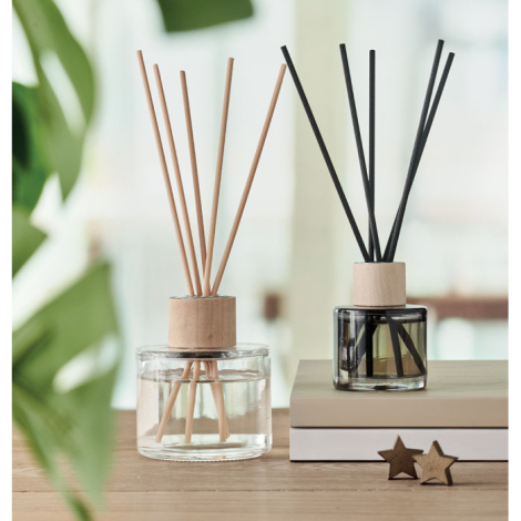 Deux diffuseurs d’arômes posés sur une table, l’un en verre transparent avec tiges bois naturel, l’autre en verre teinté gris av