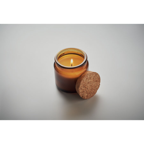 Bougie ambre en cire végétale dans un pot en verre teinté, couvercle en liège posé à côté, bougie allumée.