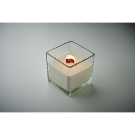 Bougie blanche en cire végétale allumée dans un pot carré en verre transparent, vue en plongée.