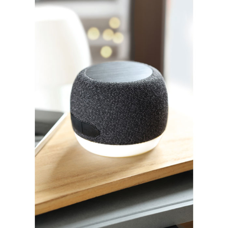 Enceinte sans fil ronde avec base blanche posée sur une surface en bois, photographiée en intérieur lumineux.