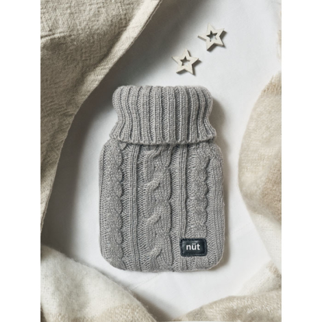 Bouillotte avec housse grise en tricot torsadé posée sur un plaid clair avec étoiles décoratives, marquage visible sur l’écusson