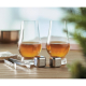 Deux verres remplis de whisky ambré sur une table avec deux cubes rafraîchissants en inox, pince en métal et pochon coton à côté