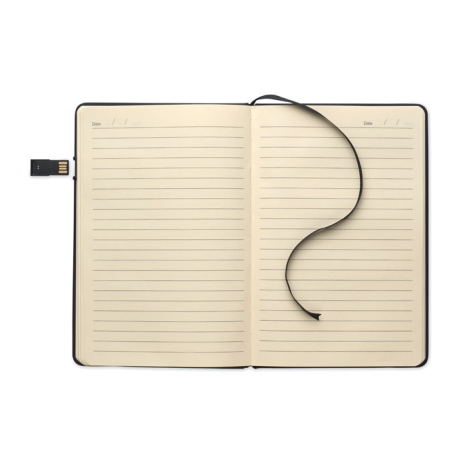 Carnet A5 ouvert à plat avec pages ivoire lignées, ruban marque-page noir et clé USB intégrée déployée sur le côté gauche.