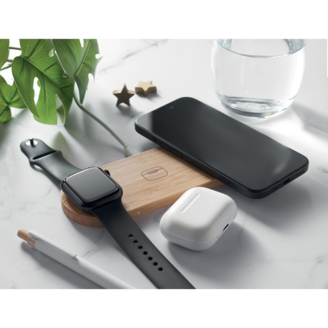 Station de charge en bambou utilisée pour recharger une montre noire, un smartphone et des écouteurs blancs.