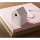 Réveil en MDF clair posé sur un livre rose avec câble blanc branché.