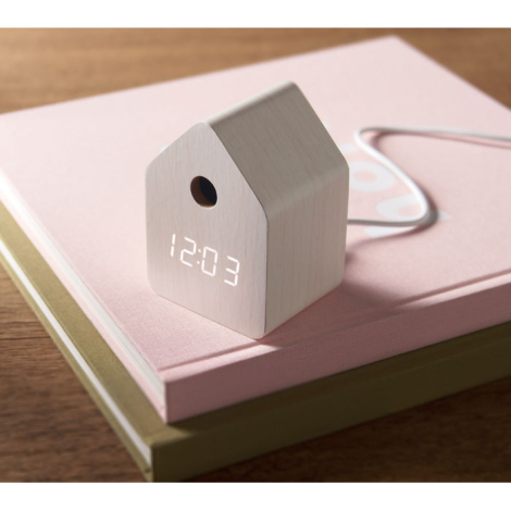Réveil en MDF clair posé sur un livre rose avec câble blanc branché.
