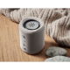 Enceinte cylindrique grise en ABS posée sur une table en bois, grille en tissu et surface supérieure en métal, marquage visible 