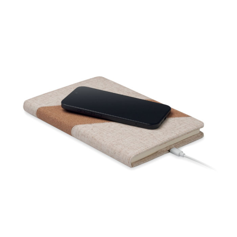Carnet A5 beige avec bande en liège utilisé comme chargeur sans fil avec smartphone noir posé dessus et câble branché.
