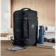 Sac de voyage noir posé sur une table en bois avec gourde et tablette, marquage visible sur la face avant et sur la poche latéra