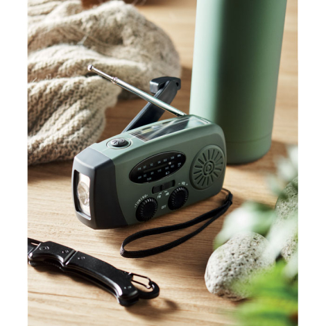 Radio portable verte en situation avec antenne déployée et manivelle relevée.