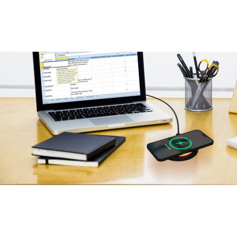 Smartphone posé sur chargeur circulaire noir branché affichant écran de charge, posé sur bureau avec ordinateur portable et four