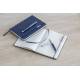 Ensemble carnet bleu marine fermé et ouvert, pages lignées avec ruban marque-page, marquage visible sur le stylo.