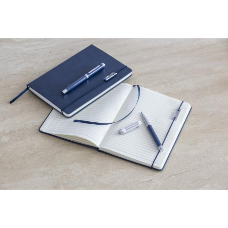 Ensemble carnet bleu marine fermé et ouvert, pages lignées avec ruban marque-page, marquage visible sur le stylo.