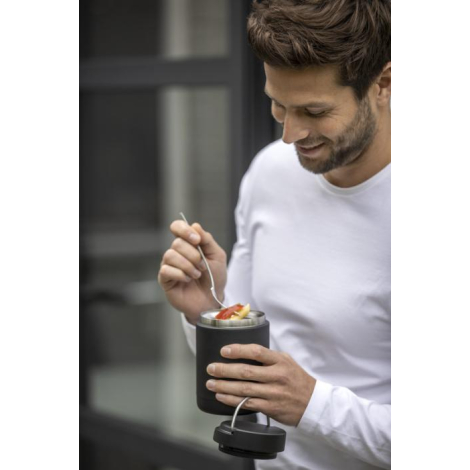 Homme tenant une boîte-repas noire ouverte et dégustant son contenu avec une cuillère.