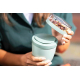 Lunch box compacte vert sauge tenue dans les mains, partie supérieure transparente contenant des fruits secs.