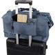 Sac bleu fixé sur la poignée d’une valise, poche avant ouverte contenant un carnet et des stylos, sans personnalisation visible.