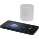 Enceinte blanche posée près d’un smartphone noir en lecture musicale, sans marquage visible.