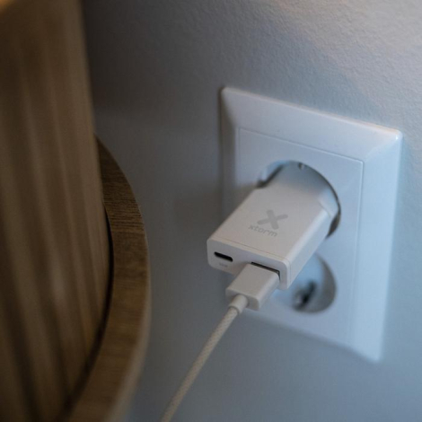 Chargeur Xtorm blanc branché sur une prise murale avec câble connecté à l’un des ports, sans personnalisation visible.