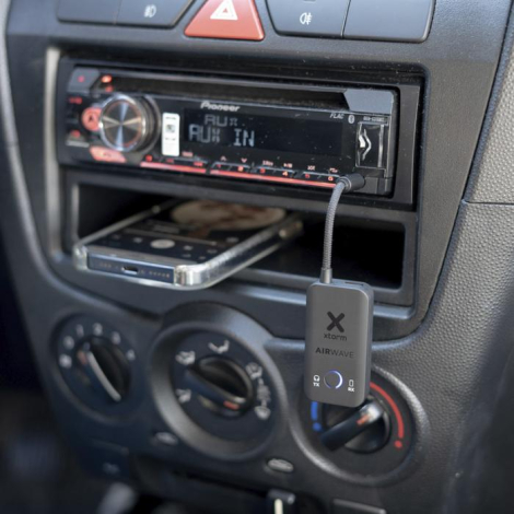 Adaptateur audio Xtorm noir branché sur prise auxiliaire d’un autoradio, visible dans l’habitacle d’un véhicule, sans personnali